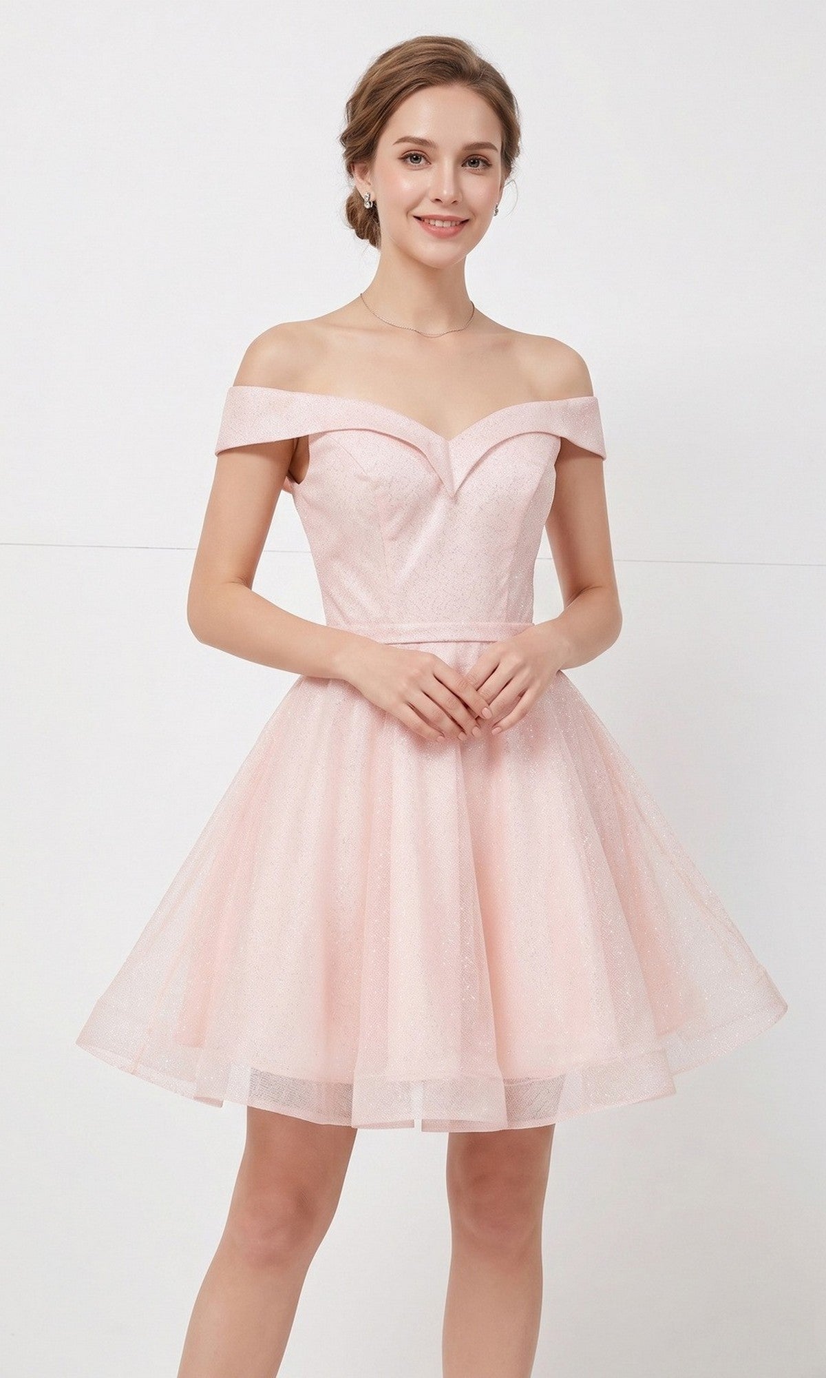 A woman wearing the Chicas C323 short homecoming dress in blush, with an off-the-shoulder fit-and-flare silhouette and a knee-length hem, stands against a plain white background, smiling at the camera.